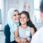 woman wearing a hijab hugging daughter sitting on her lap