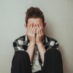teen boy sitting on floor with his face in his hands