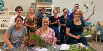 A group of mental health professionals sit in an art studio holding creations made from branches and flowers, smiling for a photo.