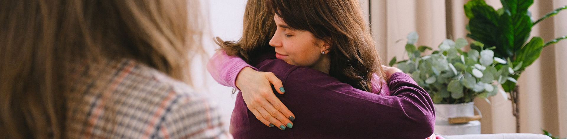 Two women share a loving embrace while sitting in a room with a therapist.