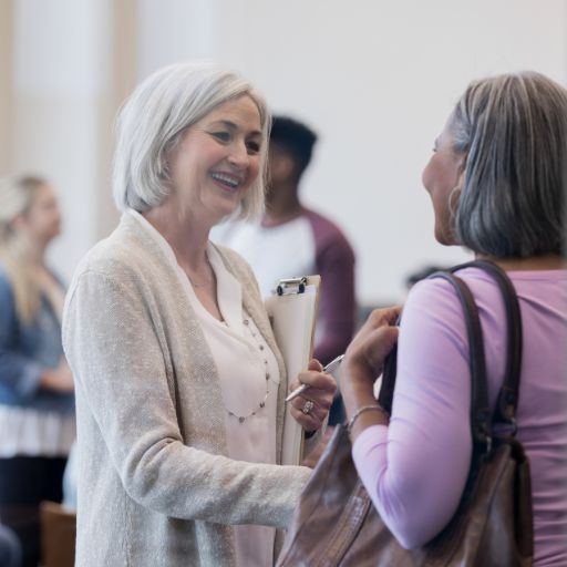 W woman holding a clipboard is shaking hands with another woman and smiling