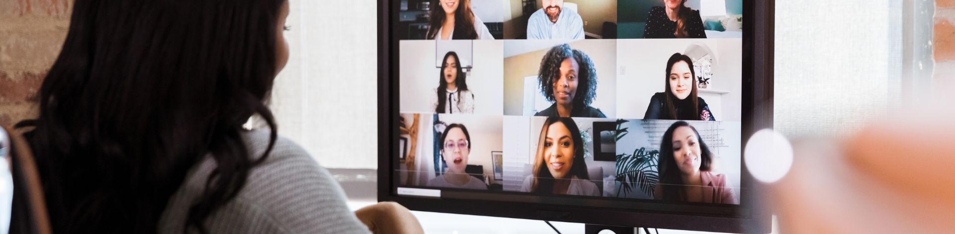 A woman faces a computer screen with a grid of peoples faces on it in an online meeting