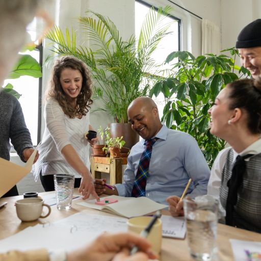 A group of professionals gather round a table all looking at a document, smiling and talking.